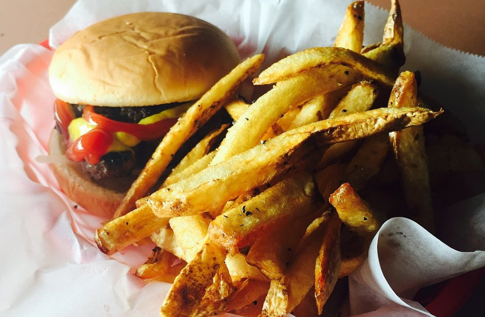 Image of a hamburger with ketchup and mustard served with a side of french fries on a basket